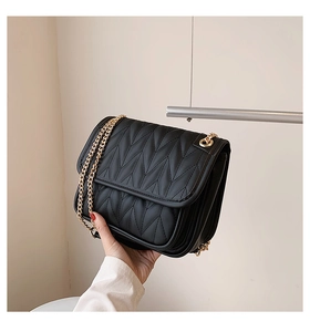 Detail of black quilted crossbody bag with V-shaped stitching and gold chain strap