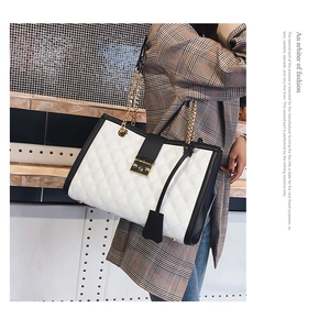 Sac bandoulière matelassé blanc avec bordure noire et chaîne dorée porté par un mannequin