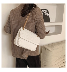 Close-up of elegant white quilted shoulder bag with gold chain strap on a model