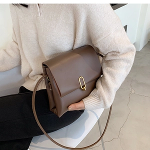 Detailed side view of a minimalist dark brown matte leather crossbody bag with gold buckle