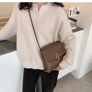 Detail of a brown leather crossbody bag featuring a stylish gold U-shaped buckle detail