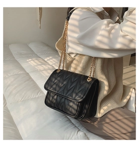 Detail of black quilted chain bag with gold hardware shown in warm indoor lighting