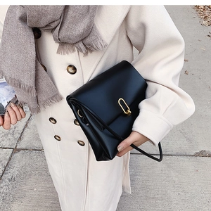 Close-up of black matte leather crossbody bag with golden oval clasp on a winter coat