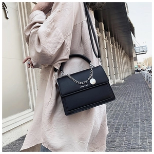 Détail d'un sac bandoulière noir élégant avec chaîne métallique et imprimé de lettres