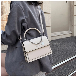 Détail d'un sac bandoulière en cuir crème avec chaîne argentée sur une veste grise