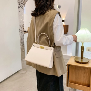 Sac à main trapèze blanc crème élégant avec boucle dorée porté à l'épaule par un mannequin