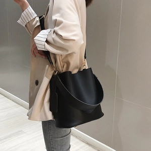 Minimalist black matte leather bucket bag with wide strap worn by a model in a beige suit