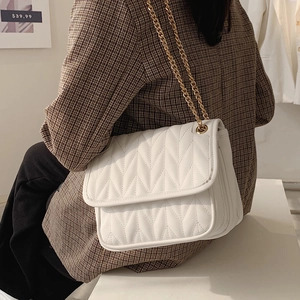 Fashionable white quilted crossbody bag with gold chain strap on shoulder