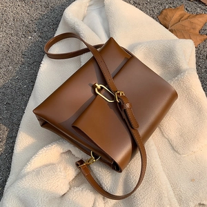 Vintage brown leather crossbody square bag with gold oval lock on a white fleece jacket