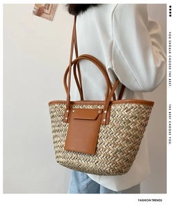 Detail of hand-woven straw tote bag with brown leather trim and front pocket design