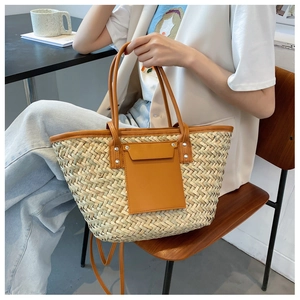 Detail of woven straw tote bag featuring brown leather pocket and handles in a lifestyle setting