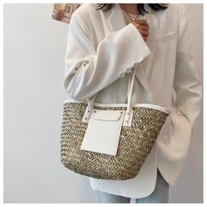 Detail of woven straw tote bag with white leather straps held by a model in white blazer