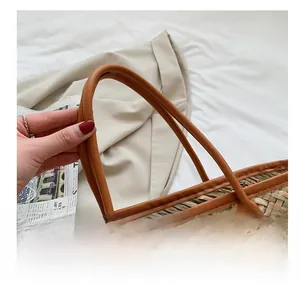 Detail of woven straw bag showing brown leather handle with silver metal rivets