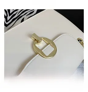 Detail shot of a white leather handbag featuring a golden geometric metal lock closure