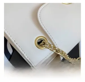 Detail of white leather shoulder bag featuring gold chain strap and metal eyelet design