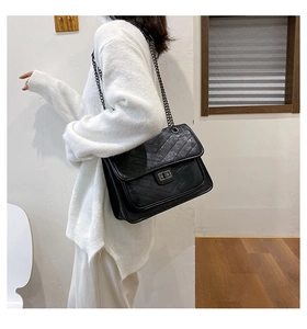 Close-up of black quilted leather shoulder bag with gold chain strap and metal turn-lock