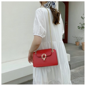 Red leather chain bag featuring gold metal buckle shown on a white dress model