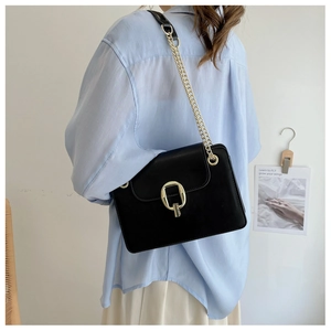 Detail of a black leather crossbody bag with gold chain strap on a female model