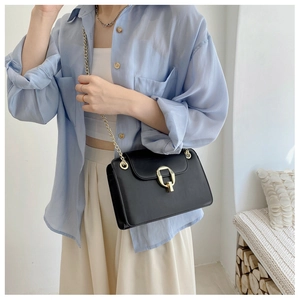 Detail of a black chain crossbody bag with gold square clasp worn by a model