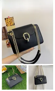 Detail of black leather crossbody bag with chunky gold chain strap and D-lock closure