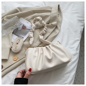 Chic beige ruched cloud bag on white sheets with minimalist lifestyle accessories
