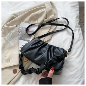 Macro shot of black pleated cloud bag texture on white bedding with soft PU leather detail