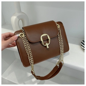 Detail of a brown leather crossbody bag featuring a gold D-ring buckle and chain strap