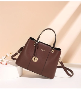 Detail of dark brown lychee texture handbag with golden text and circular metal pendant