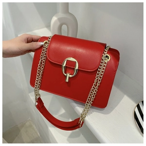 Detail of red leather crossbody bag featuring a round gold buckle and dual chain strap