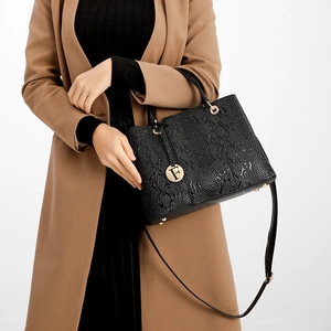 Close-up of black textured handbag with gold letter F pendant and top handle details