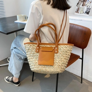 Handcrafted woven straw tote bag with brown leather handles and a front pocket for summer