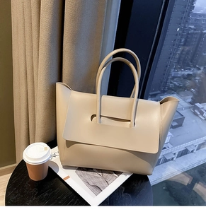 Close-up of beige tote bag with unique wide flap design on a modern office desk