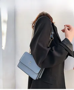 Detailed view of dusty blue crossbody bag with gold deer logo and metal chain strap