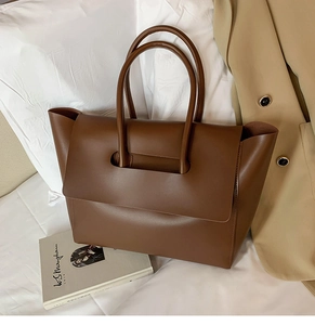 Detail of a brown leather tote bag with unique handle-through-flap design and wing shape