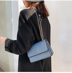 Detail of blue flap shoulder bag with metal chain strap and deer head logo emblem