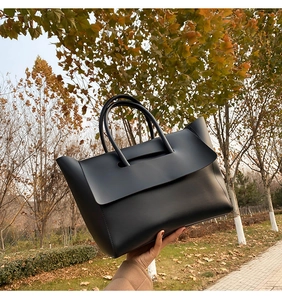 Detailed view of the sleek black leather tote bag with sturdy handles in autumn setting