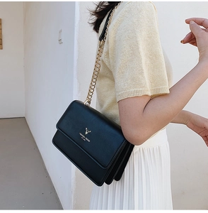 Detail of black PU leather shoulder bag with golden deer logo and metal chain strap