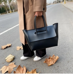 Close-up of a matte black leather tote bag with unique cut-out handles in a street setting
