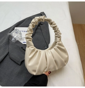 Detail of a beige pleated scrunchie handle bag on a grey blazer for a chic city style