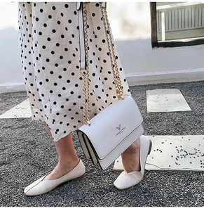 Close-up of white leather handbag featuring gold deer logo and metallic chain strap detail