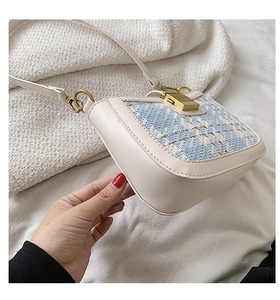 Detail of tweed flap bag with gold hardware and ivory leather strap on textured blanket