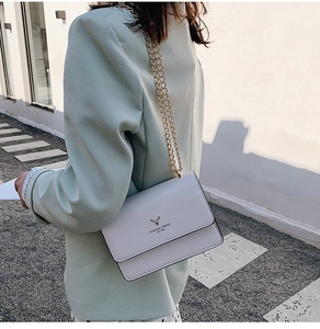 Detailed view of white crossbody bag with gold deer head logo and slim metal chain strap