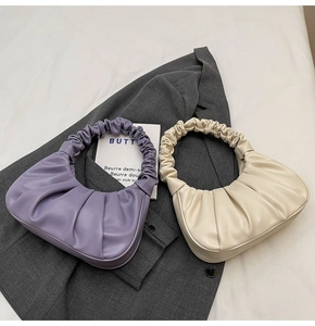 Detailed close-up of lavender and beige pleated crescent bags on a grey suit jacket