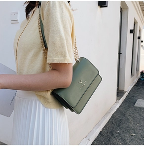 Detail of green shoulder bag featuring a gold deer head logo and metallic chain strap