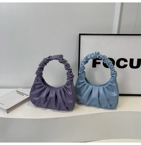 Detail view of purple and light blue cloud bags with gathered pleats on a minimal pedestal