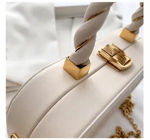 Detalle de bolso de cuero blanco con cierre dorado rectangular y asa de nudo elegante