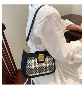 Chic black and white plaid shoulder bag worn by model sitting next to wooden table