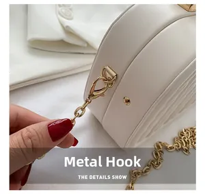 Detalle de bolso en cuero blanco texturizado con gancho dorado pulido y correa de cadena