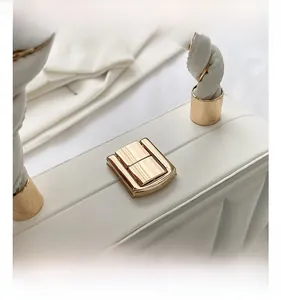 Detail of white quilted handbag featuring golden metal clasp and woven handle texture
