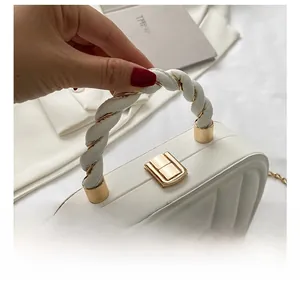 Close-up of white quilted handbag with braided handle and gold metal twist lock detail